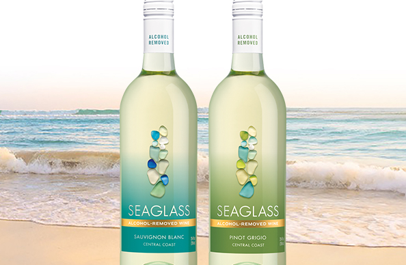 A bottle of SEAGLASS alcohol-removed pinot grigio and sauvignon blanc with the ocean behind them