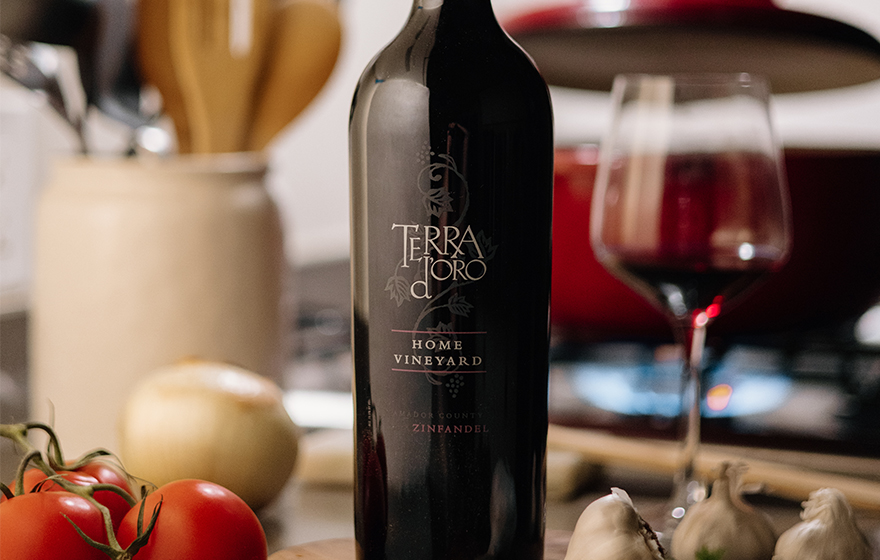 bottle and glass of terra d'oro home vineyard zinfandel next to tomatoes and garlic with a pot simmering in the background