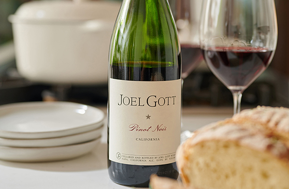 bottle and glass of joel gott pinot noir next to a loaf of bread, plates, and a white pot on a stove in the background