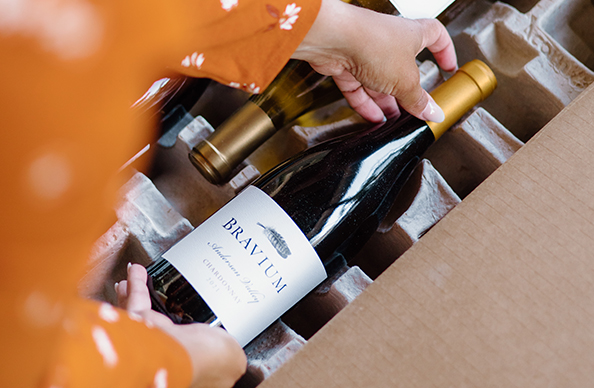 woman unboxing a One Stop Wine Shop quintessential wine club shipment featuring bravium wines