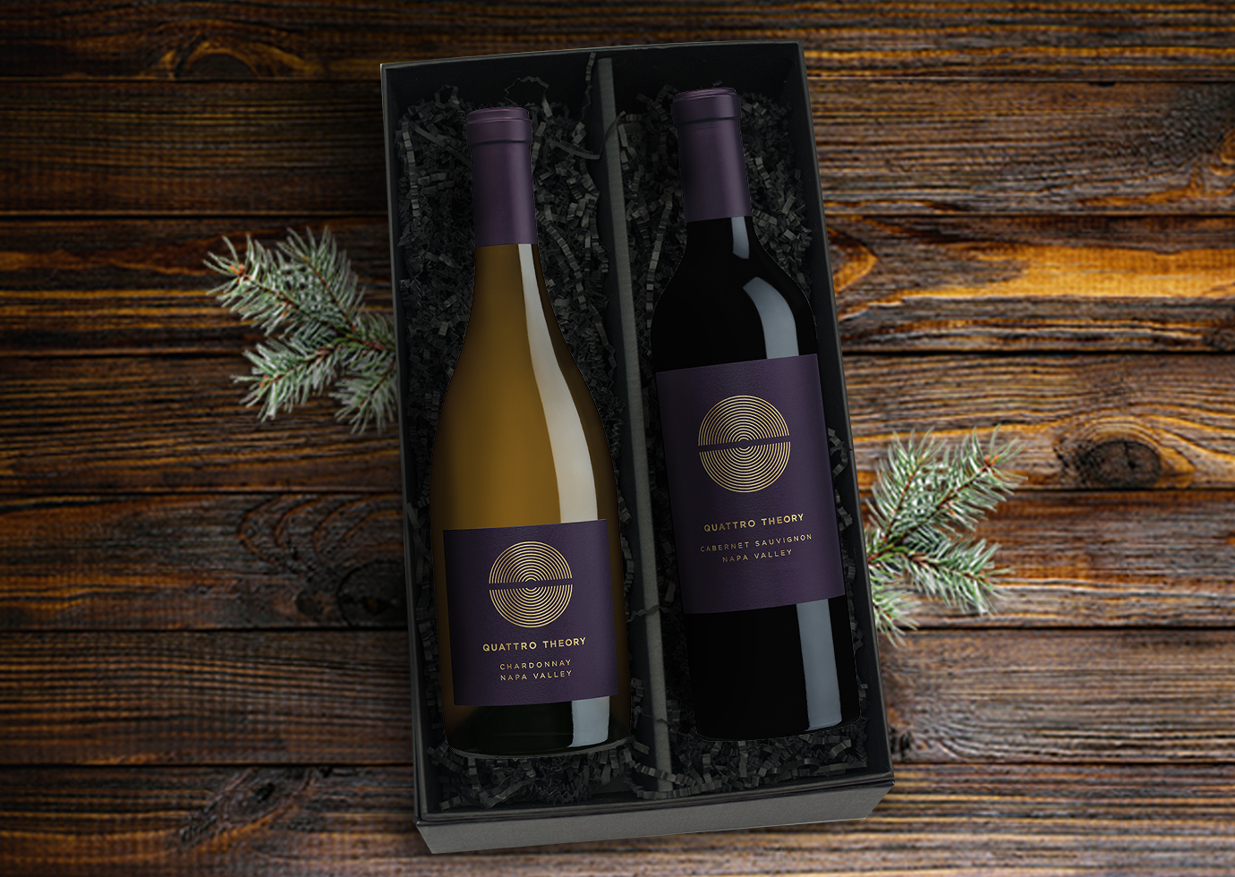 Wine gift set of two Quattro Theory wines in a black gift box on a dark wood table with sprigs of pine trees